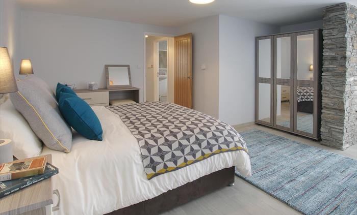 Generously sized master bedroom with modern grey furnishings, a feature stone pillar, and a cosy patterned throw.